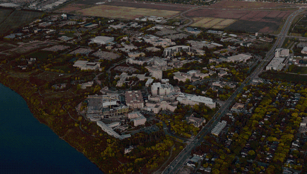 Aerial photograph of the USask campus situated beside a river, showing academic buildings, green spaces, roadways, and surrounding residential and agricultural areas.